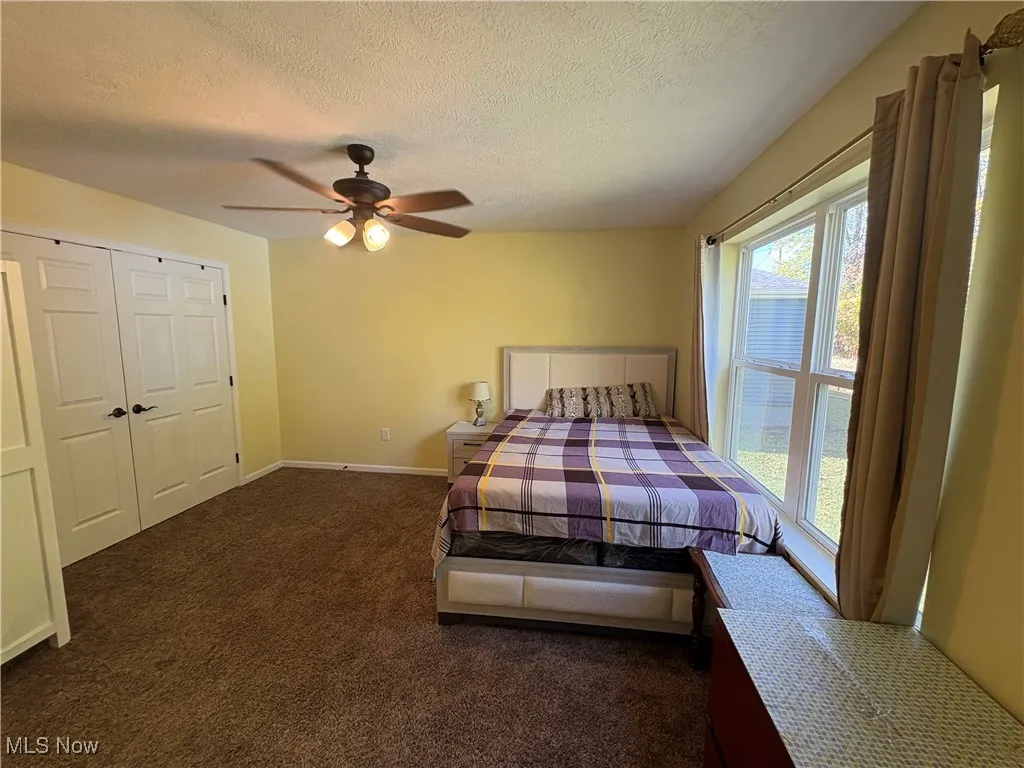 Bedroom featuring dark colored carpet, a textured ceiling, a ceiling fan, and a closet