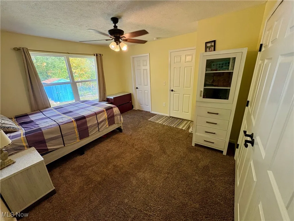Bedroom with dark carpet, access to outside, a textured ceiling, ceiling fan, and multiple closets