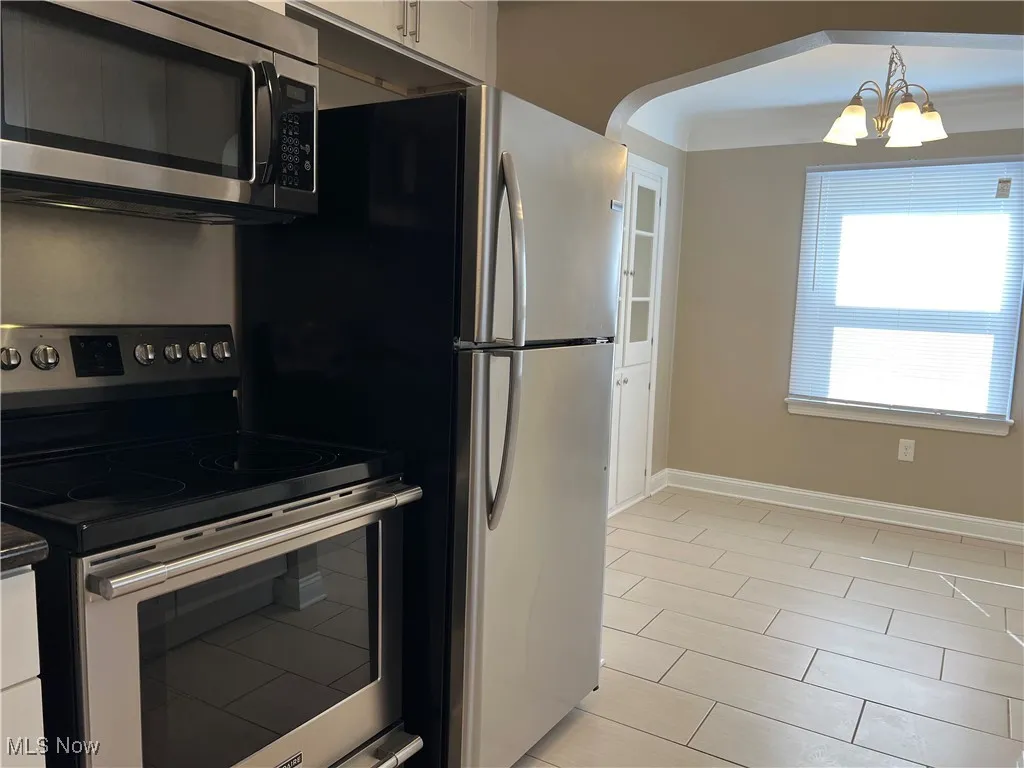 Kitchen featuring stainless steel appliances, white cabinets, a chandelier, light tile patterned flooring, and dark countertops