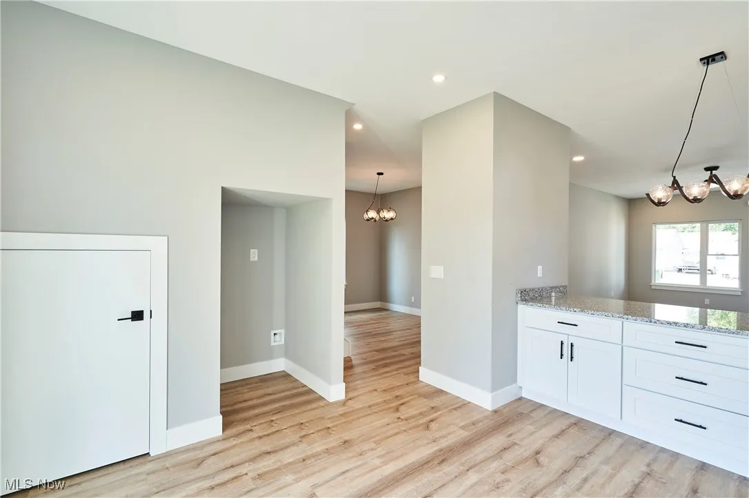 Kitchen with light wood-type flooring, pendant lighting, white cabinets, light stone counters, and a notable chandelier