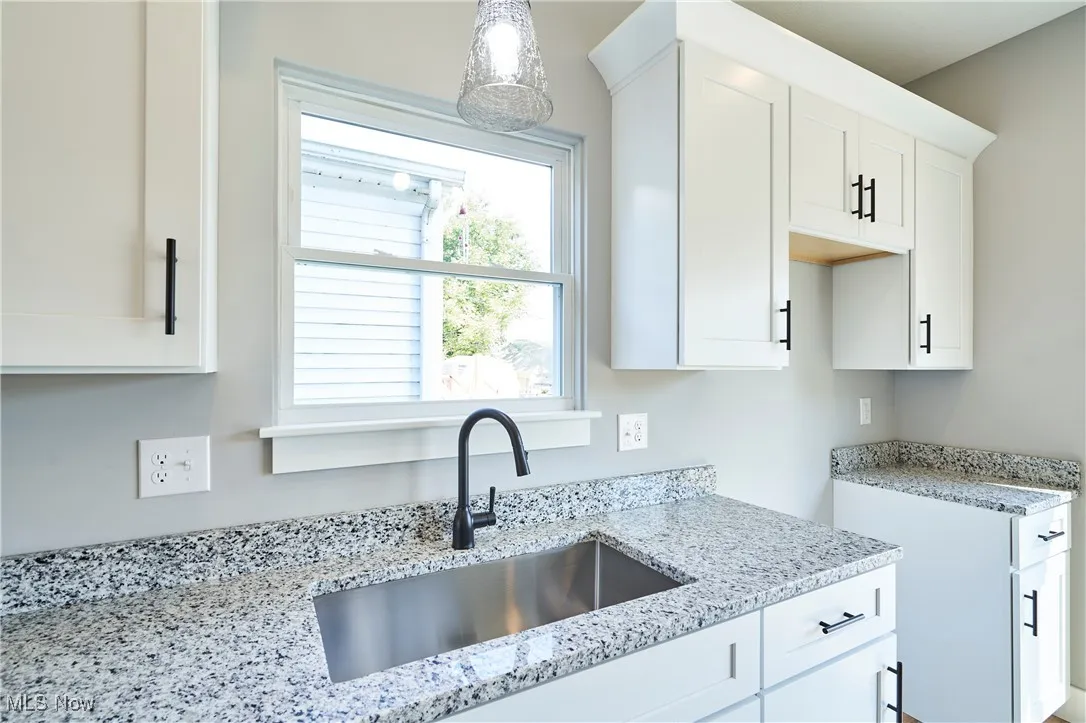 Kitchen featuring light stone counters, sink, pendant lighting, and white cabinets
