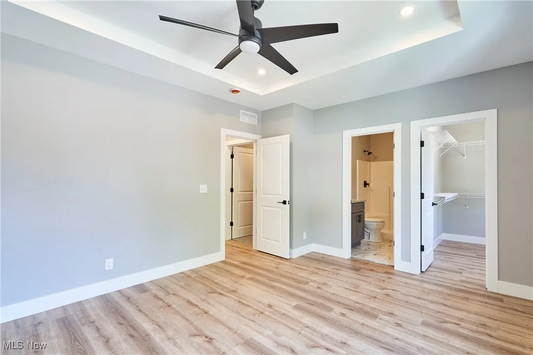 Unfurnished bedroom featuring light hardwood / wood-style flooring, ceiling fan, a walk in closet, and ensuite bath