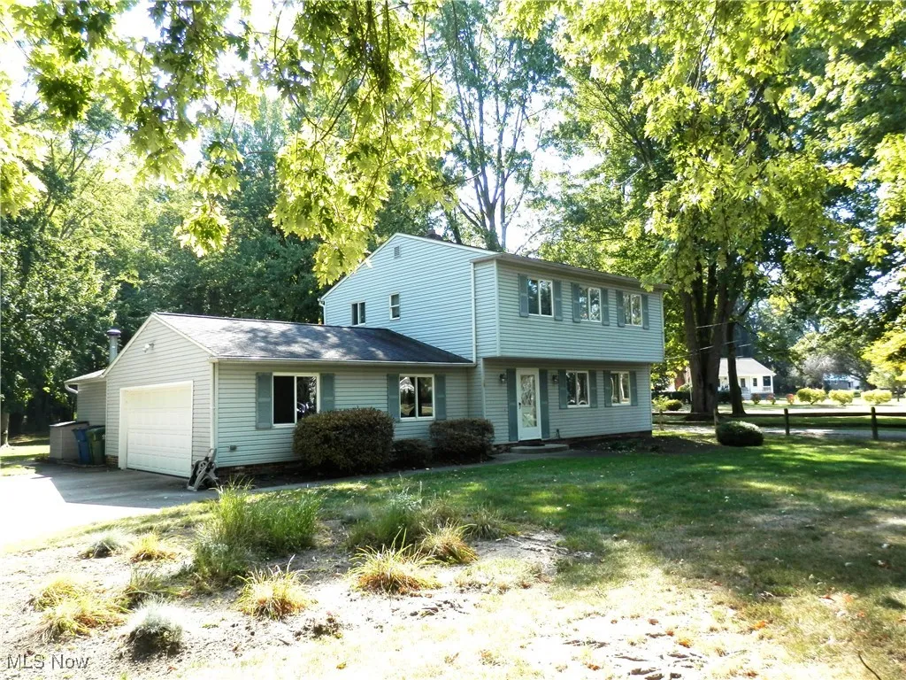 Colonial-style house with a garage, view of scattered trees, and driveway