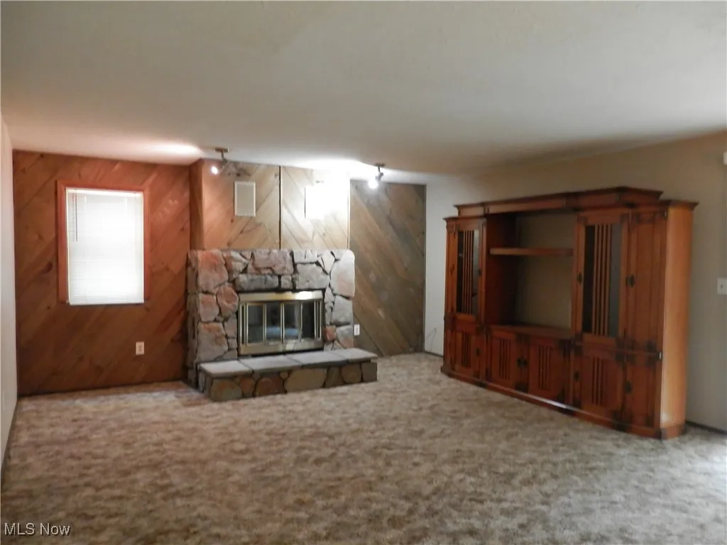Unfurnished living room with a fireplace, wood walls, and carpet flooring