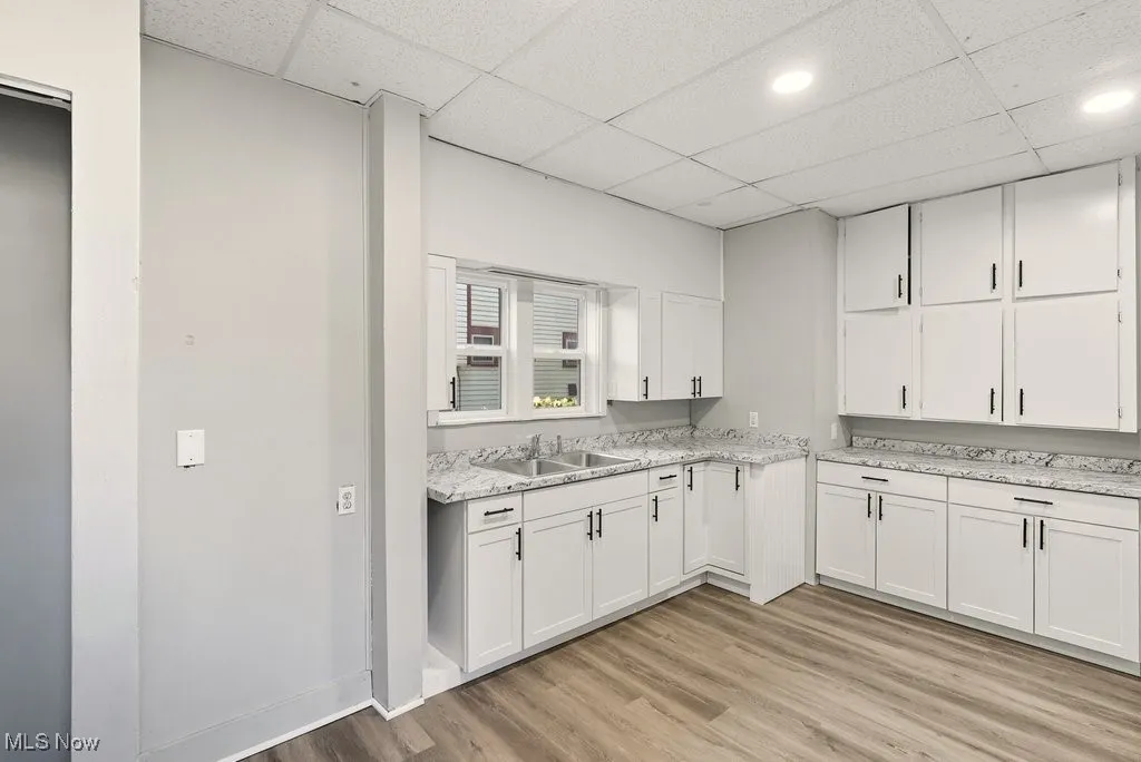 Kitchen with a drop ceiling, white cabinets, and light wood-style floors