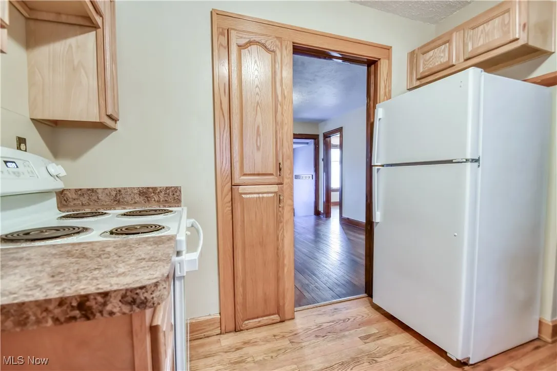Kitchen with white appliances, light wood-style floors, light countertops, a textured ceiling, and light brown cabinetry