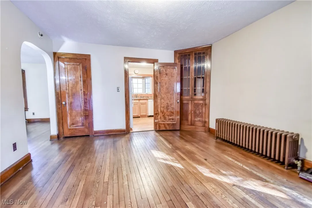 Unfurnished room with radiator heating unit, hardwood / wood-style flooring, arched walkways, and a textured ceiling