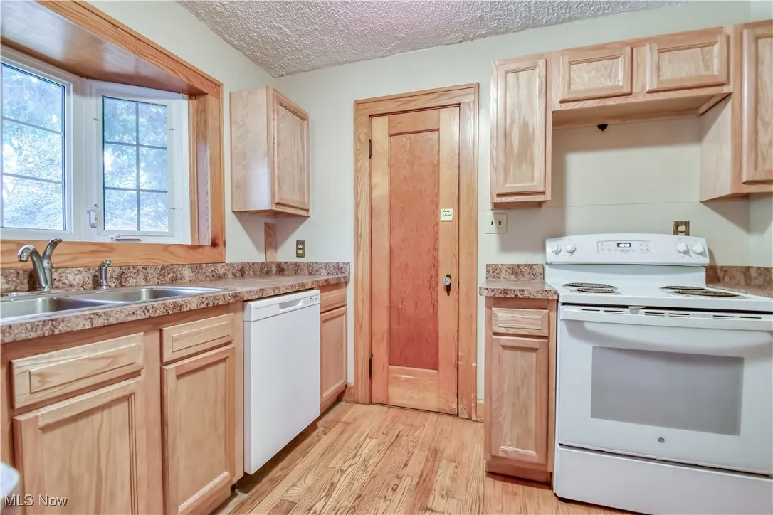 Kitchen with light brown cabinets, white appliances, light wood-style flooring, light countertops, and a textured ceiling