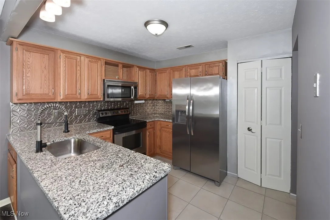 Kitchen featuring appliances with stainless steel finishes, decorative backsplash, light stone countertops, light tile patterned floors, and a textured ceiling