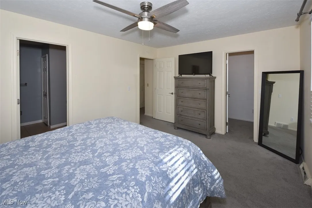 Bedroom with carpet flooring, a textured ceiling, ceiling fan, and ensuite bath
