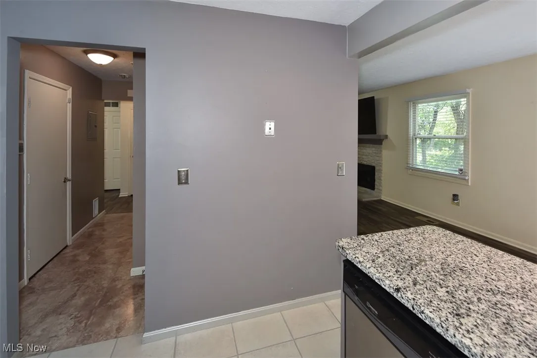 Kitchen with light stone counters, light tile patterned floors, a stone fireplace, dishwasher, and dark cabinetry