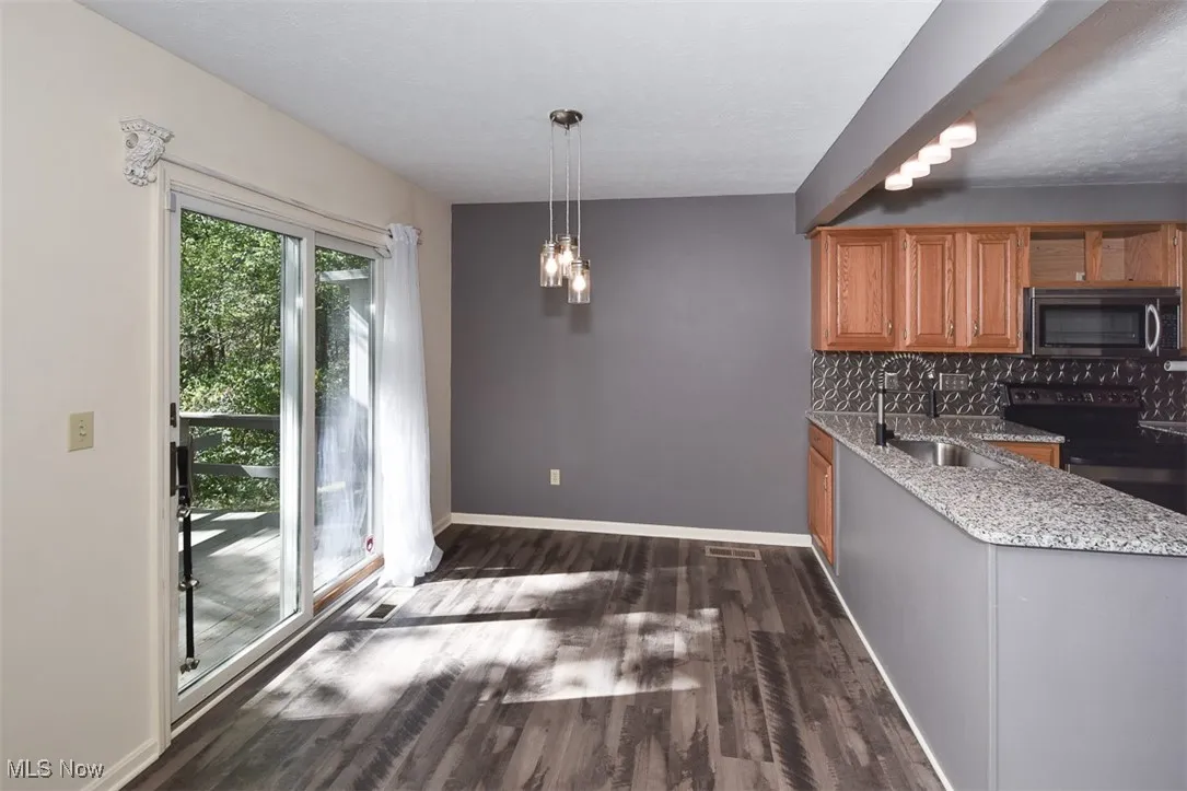 Kitchen with decorative backsplash, black electric range, dark wood-style floors, stainless steel microwave, and light stone countertops