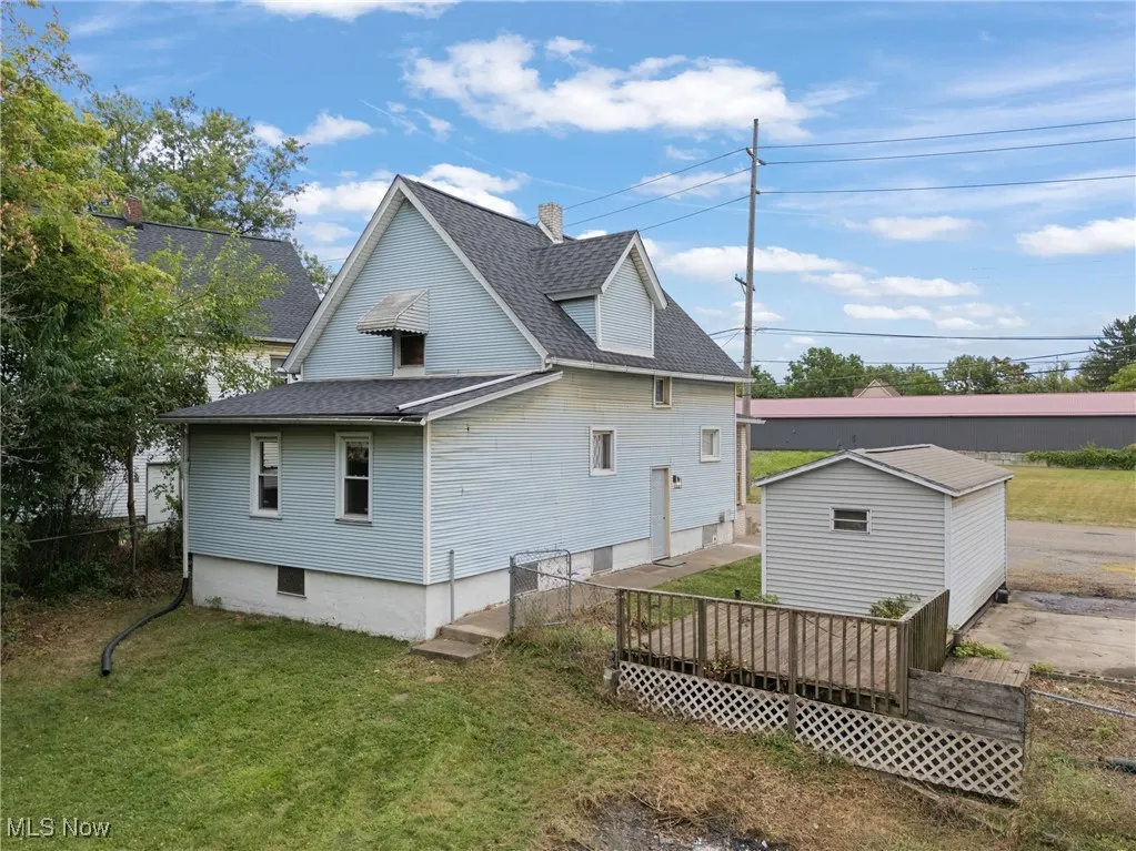 Rear view of property with a deck, roof with shingles, and an outbuilding