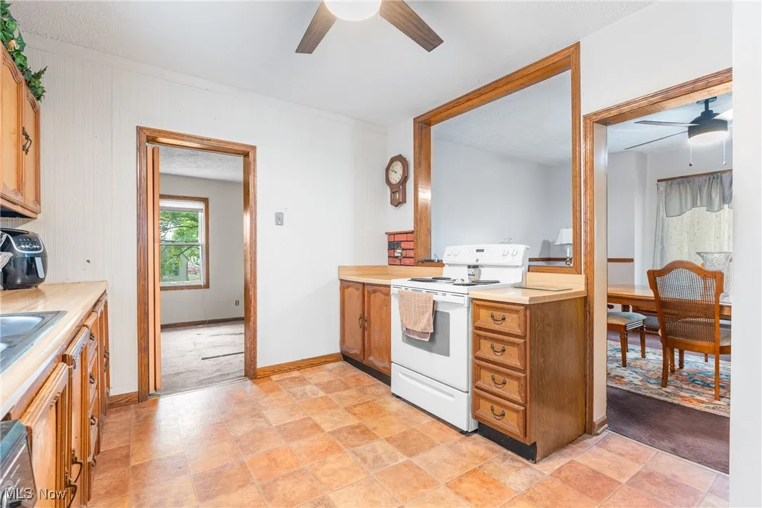 Kitchen with a ceiling fan, white electric stove, light countertops, and brown cabinets