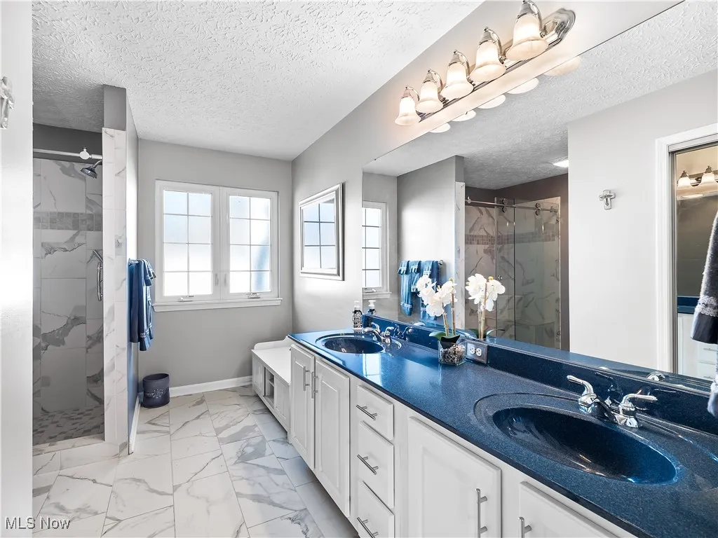 Full bath featuring a marble finish shower, light marble finish flooring, double vanity, and a textured ceiling