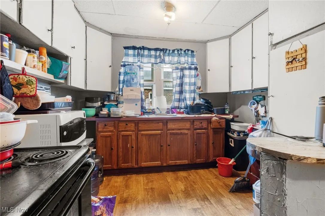 Kitchen with light wood-style flooring, white cabinetry, white microwave, brown cabinets, and black electric range