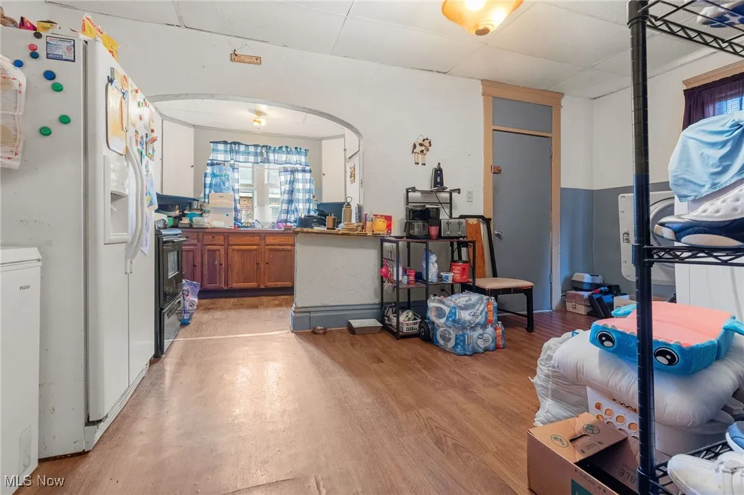 Kitchen featuring brown cabinets, white refrigerator with ice dispenser, a drop ceiling, light wood-type flooring, and black range with electric cooktop