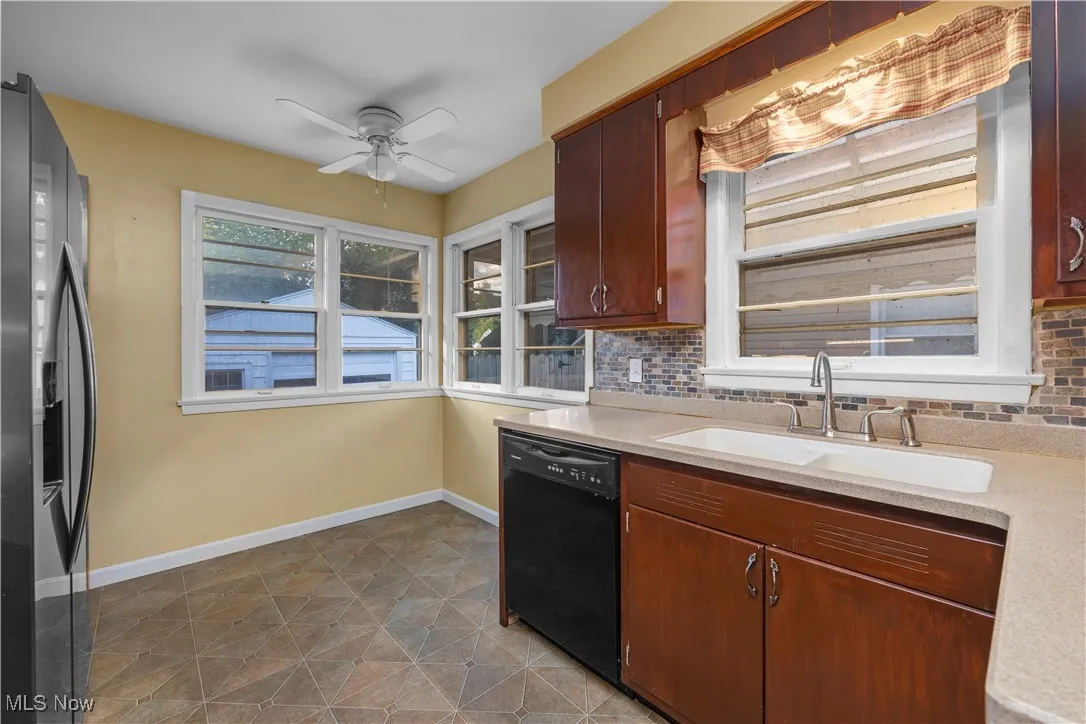 Kitchen with refrigerator with ice dispenser, black dishwasher, decorative backsplash, a ceiling fan, and light stone countertops