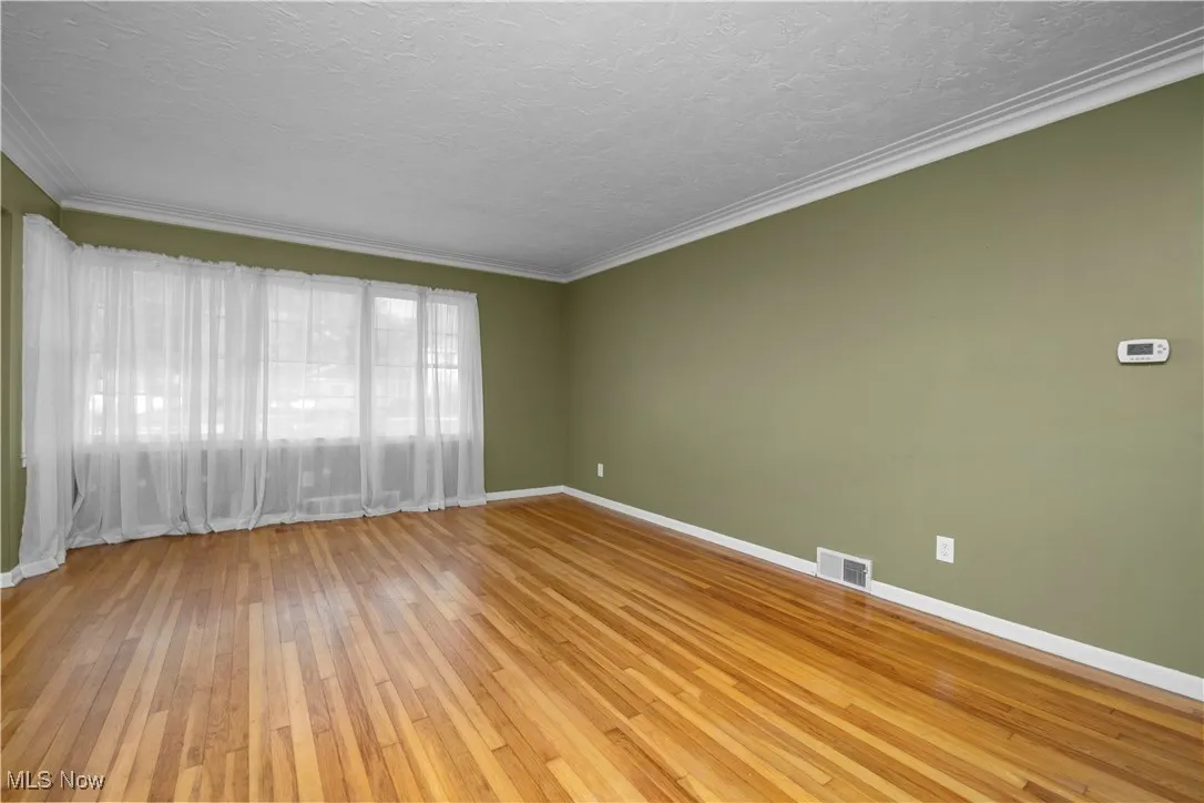 Unfurnished room featuring light wood-style flooring, crown molding, and a textured ceiling