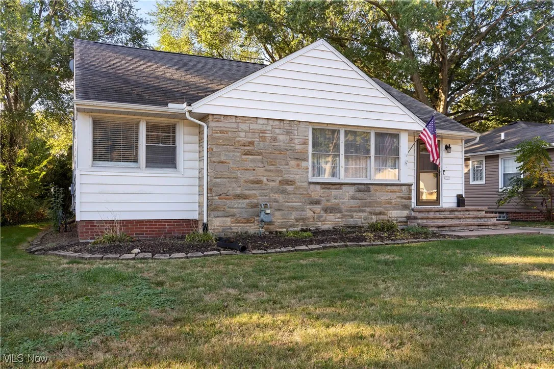 View of front of house with a front yard, roof with shingles, and stone siding