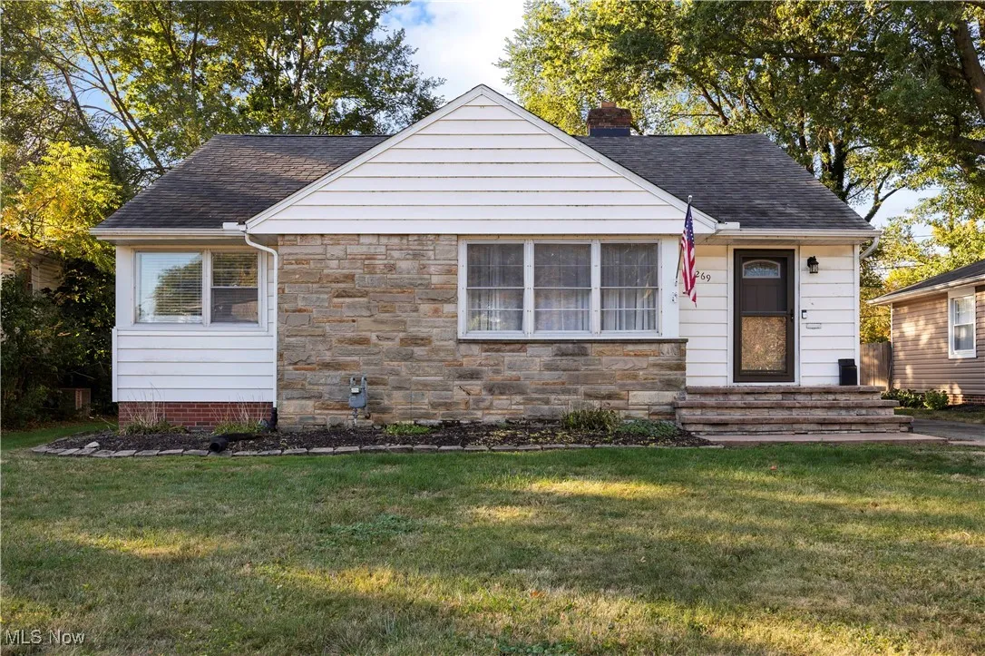 View of front facade with a front yard, a chimney, stone siding, and a shingled roof
