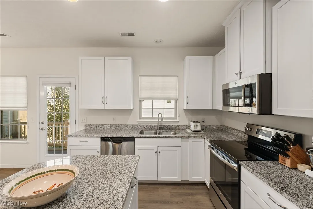 Kitchen featuring appliances with stainless steel finishes, white cabinets, dark wood-type flooring, light stone counters, and recessed lighting