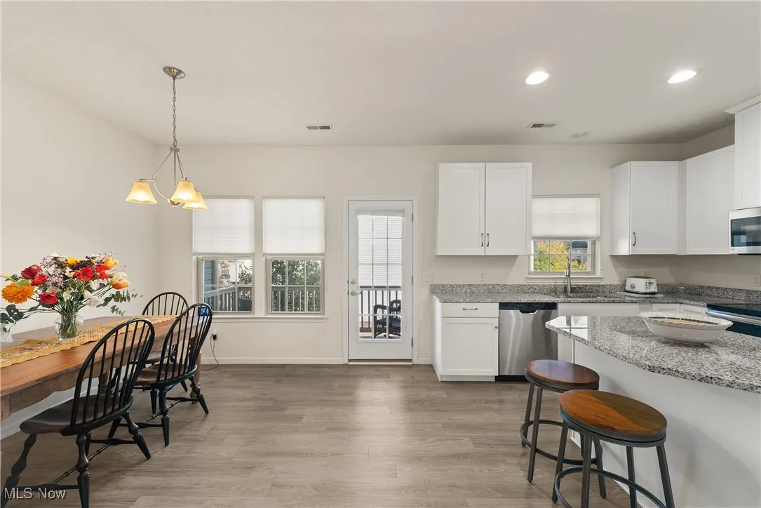 Kitchen with light stone counters, white cabinetry, recessed lighting, hanging light fixtures, and light wood-style flooring