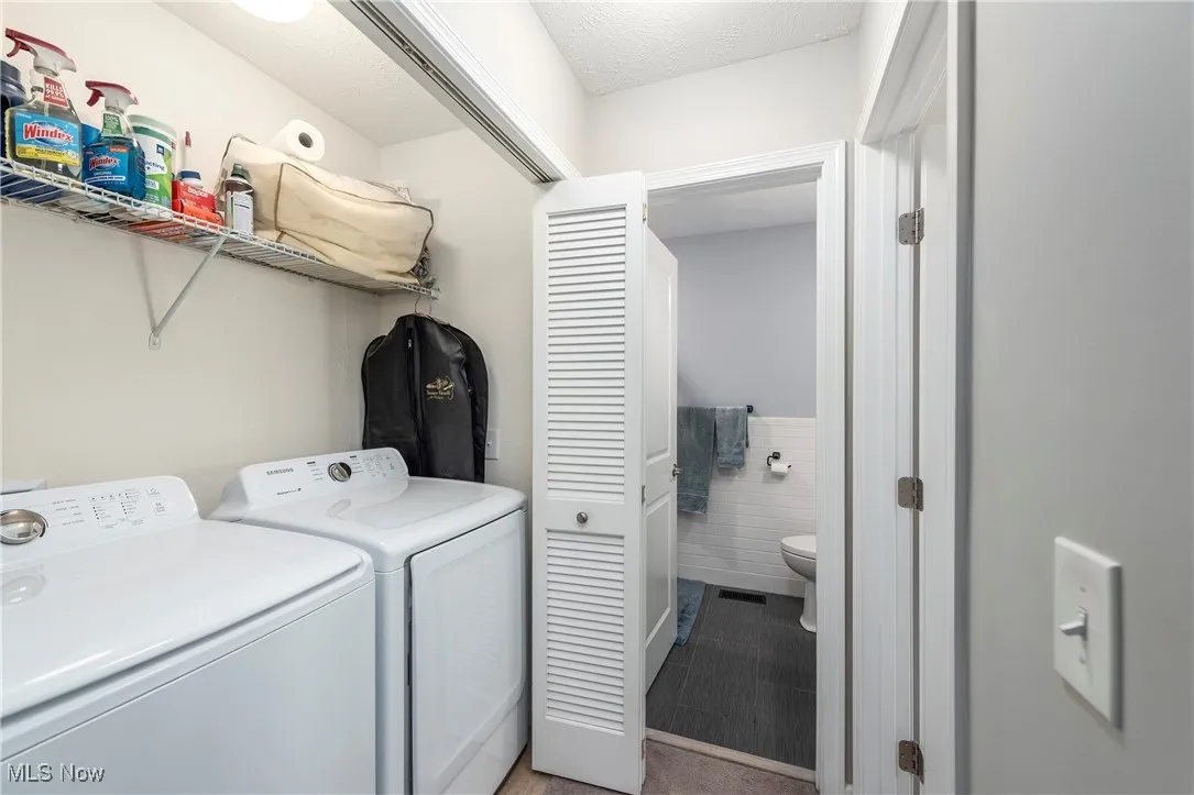 Laundry room featuring tile walls, independent washer and dryer, and a wainscoted wall
