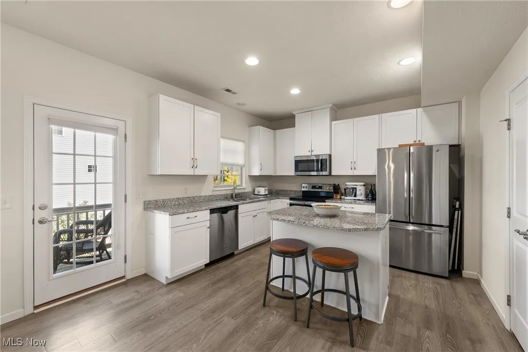 Kitchen with stainless steel appliances, light stone counters, white cabinets, recessed lighting, and a kitchen bar