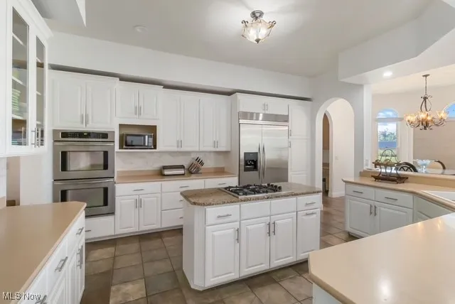 Kitchen featuring a kitchen island, appliances with stainless steel finishes, light countertops, decorative light fixtures, and white cabinetry