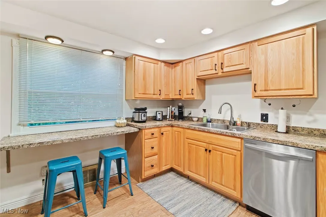 Kitchen with light brown cabinets, stainless steel dishwasher, light wood finished floors, recessed lighting, and light stone countertops