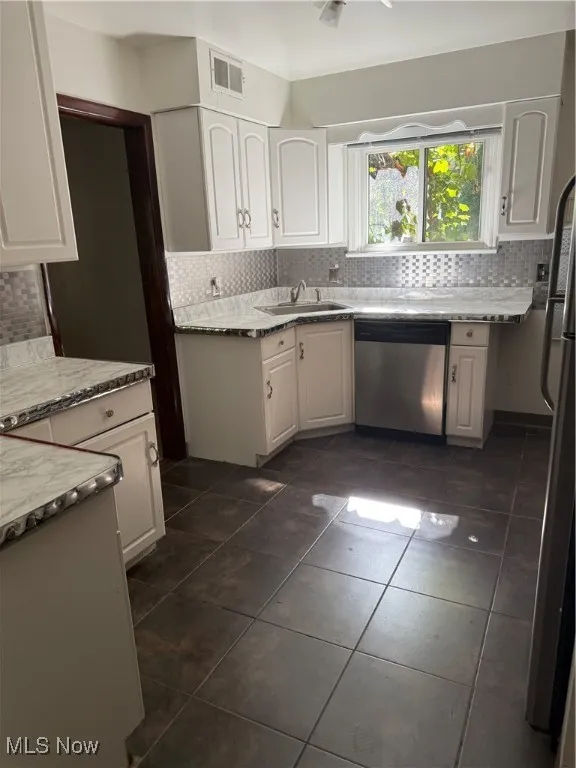 Kitchen with tasteful backsplash, white cabinets, dishwasher, and dark tile patterned floors