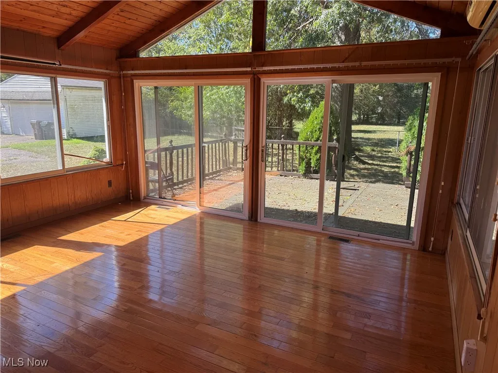 Unfurnished sunroom featuring wood walls, hardwood / wood-style floors, healthy amount of natural light, and wooden ceiling