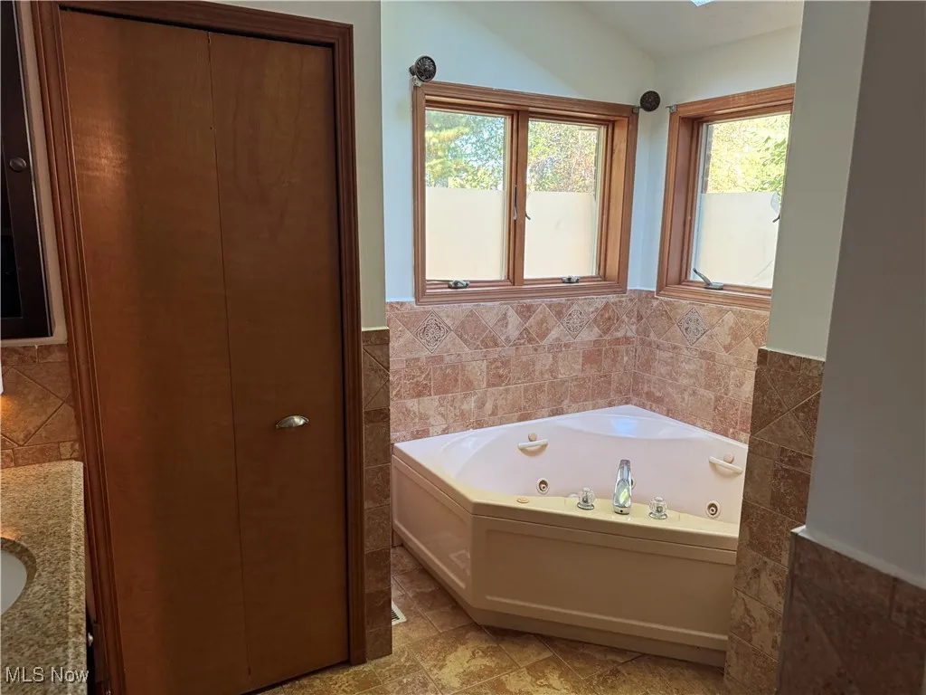 Master Bathroom featuring tile walls, a whirlpool tub, a wainscoted wall, plenty of natural light, and vanity