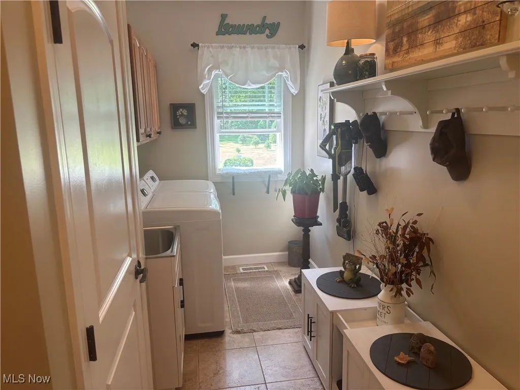 first floor laundry room featuring light tile patterned floors, cabinet space, and washer and clothes dryer