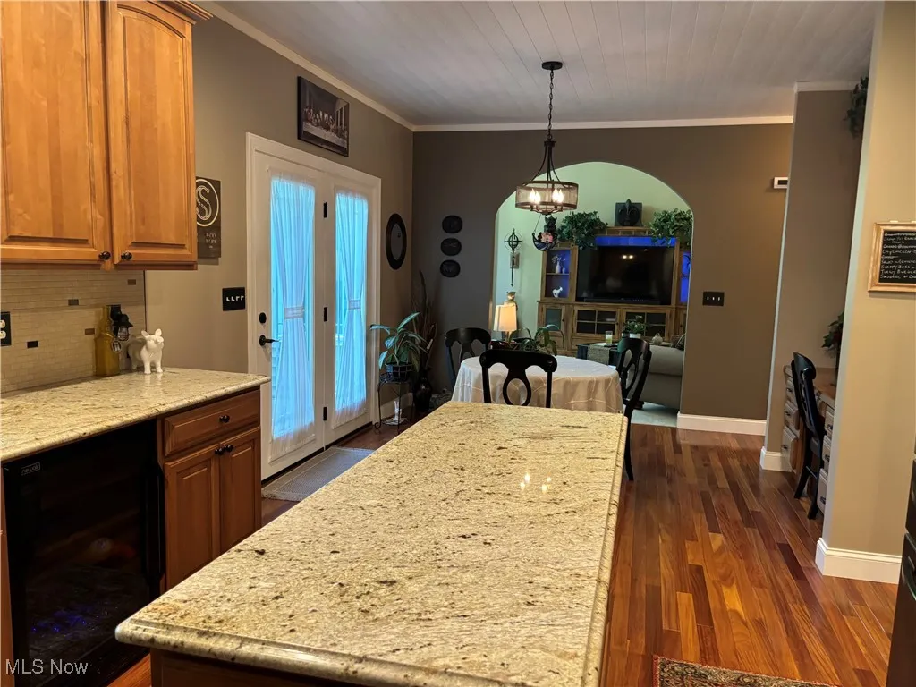 Kitchen featuring beverage cooler, dark wood-style floors, ornamental molding, light stone counters, and arched walkways