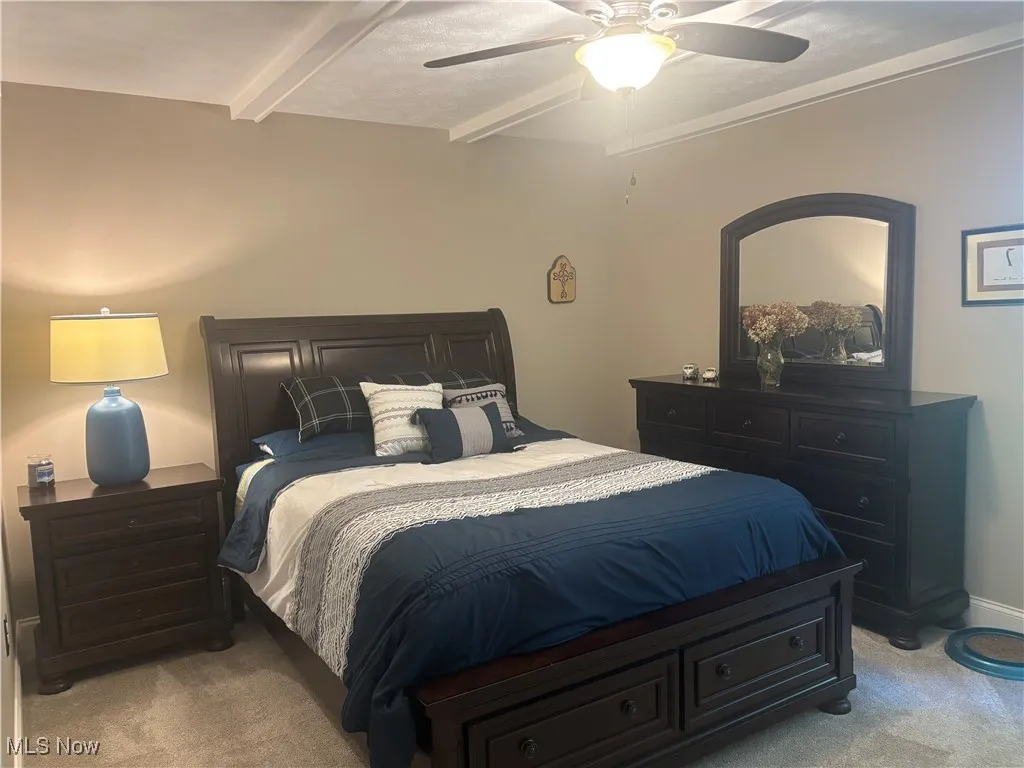 Bedroom with beamed ceiling, carpet, ceiling fan, and a textured ceiling