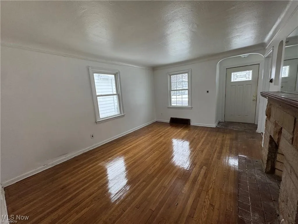 Unfurnished living room featuring dark wood-type flooring, healthy amount of natural light, a textured ceiling, and ornamental molding