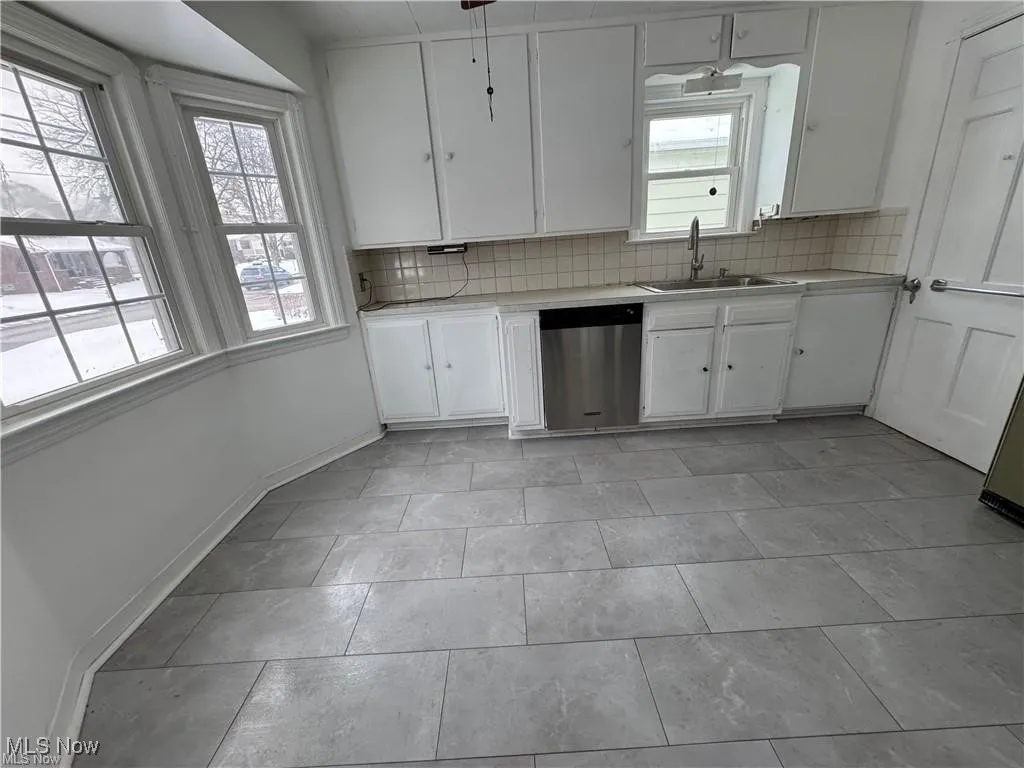 Kitchen featuring white cabinets, decorative backsplash, stainless steel dishwasher, and tile countertops