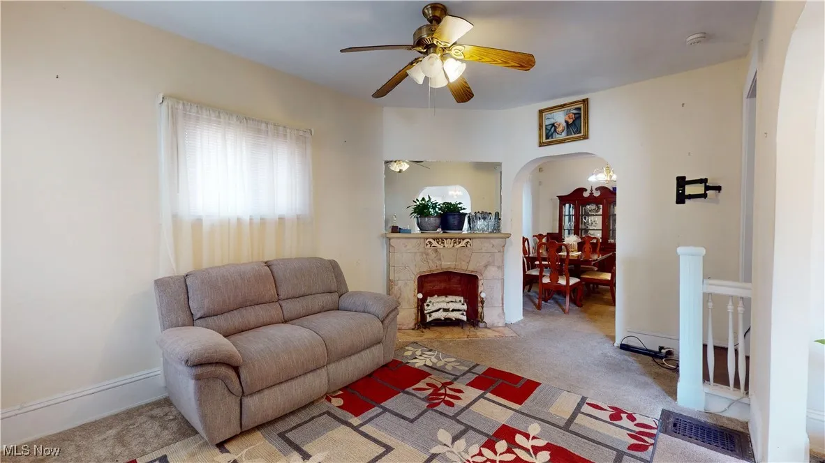 Living room with a ceiling fan, a tile fireplace, arched walkways, and carpet