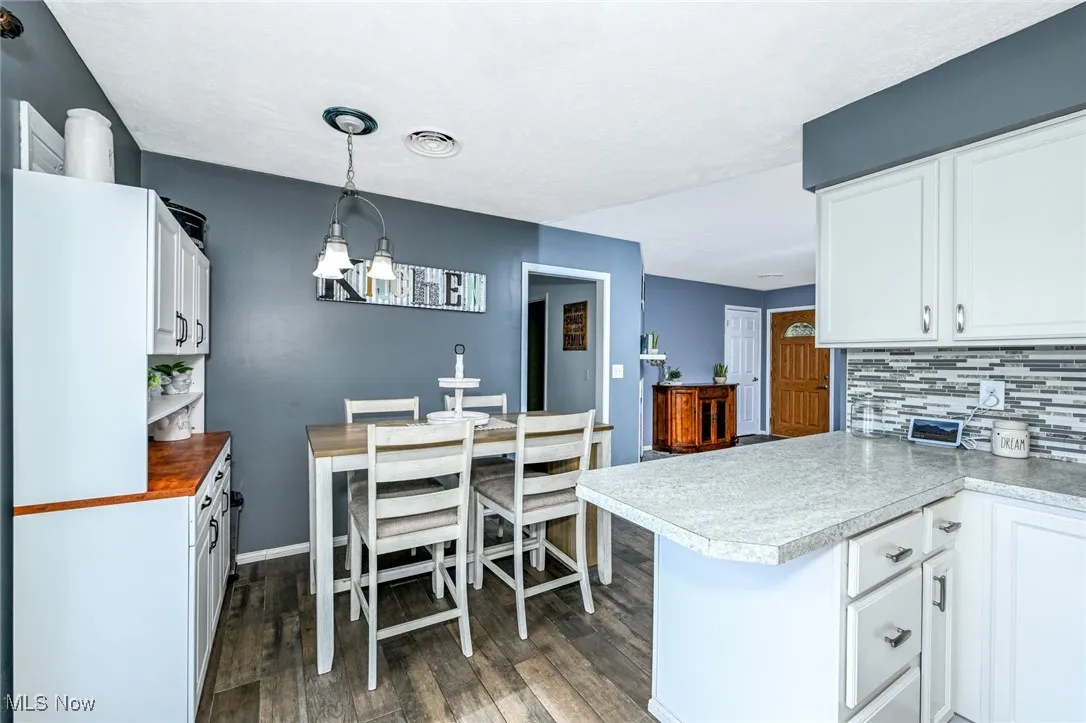 Kitchen featuring decorative backsplash, white cabinets, dark wood finished floors, and light countertops