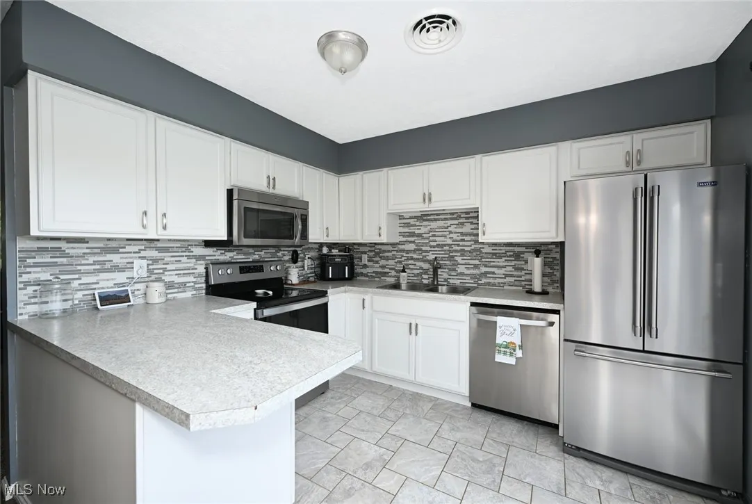 Kitchen featuring appliances with stainless steel finishes, a peninsula, white cabinetry, light countertops, and tasteful backsplash