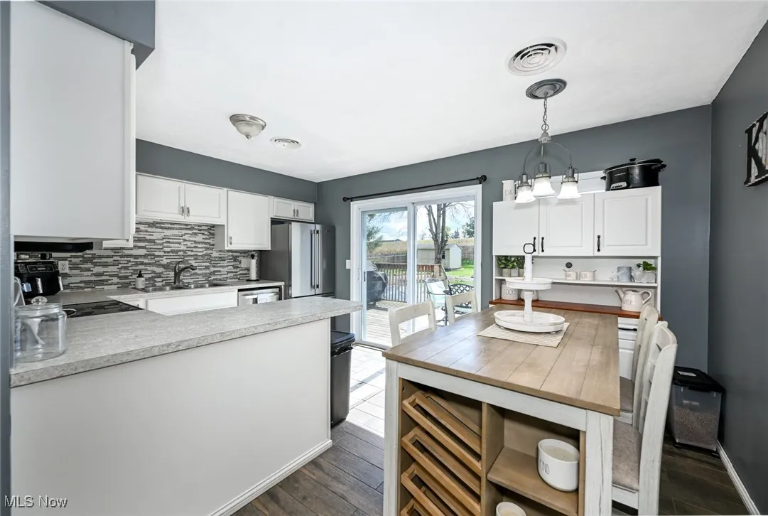 Kitchen with light countertops, decorative backsplash, a peninsula, pendant lighting, and white cabinets