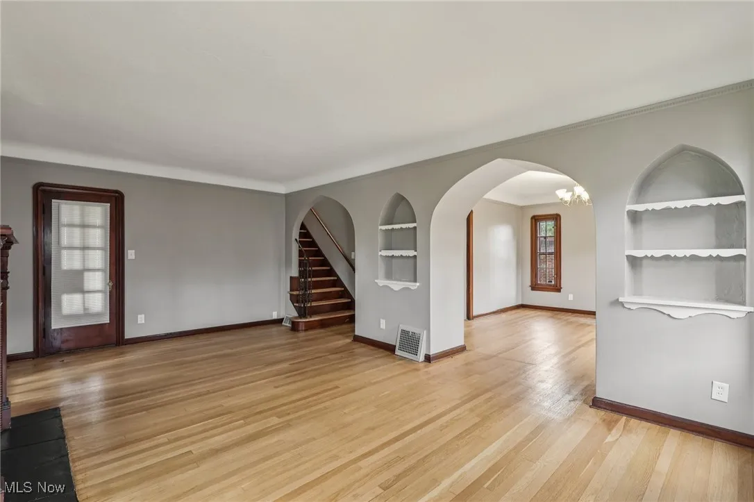 Unfurnished room with built in shelves, plenty of natural light, stairs, light wood-type flooring, and crown molding