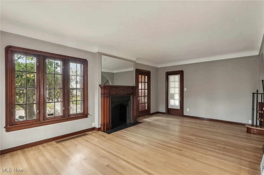 Unfurnished living room featuring a fireplace with flush hearth, light wood finished floors, and ornamental molding