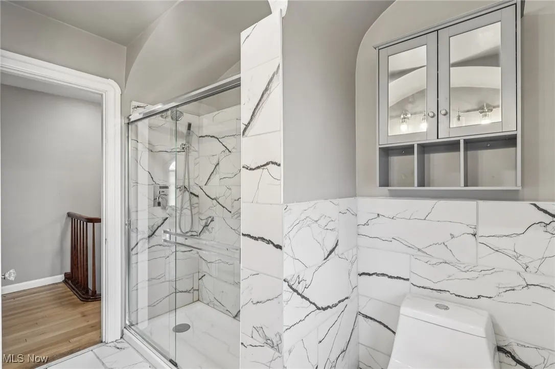 Full bath with a marble finish shower, marble look tile flooring, and tile walls