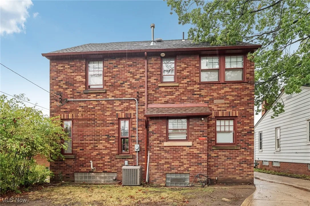 Back of property featuring brick siding and a shingled roof