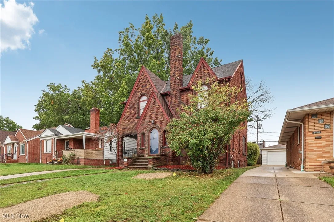 English style home featuring an outbuilding, brick siding, a chimney, and a front lawn