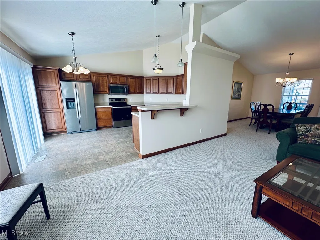 Kitchen with a chandelier, light colored carpet, hanging light fixtures, and high vaulted ceiling