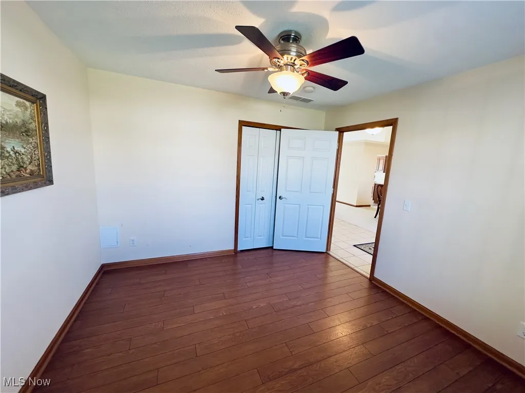 Bedroom with dark wood-type flooring, a ceiling fan, and a closet.